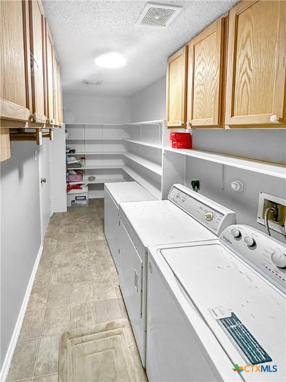 clothes washing area with cabinet space, baseboards, visible vents, washing machine and clothes dryer, and a textured ceiling