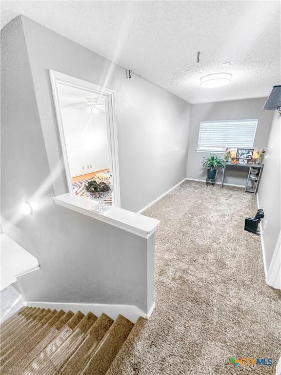 hall with carpet floors, a textured ceiling, baseboards, and stairs