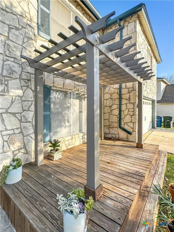 deck with driveway, an attached garage, and a pergola