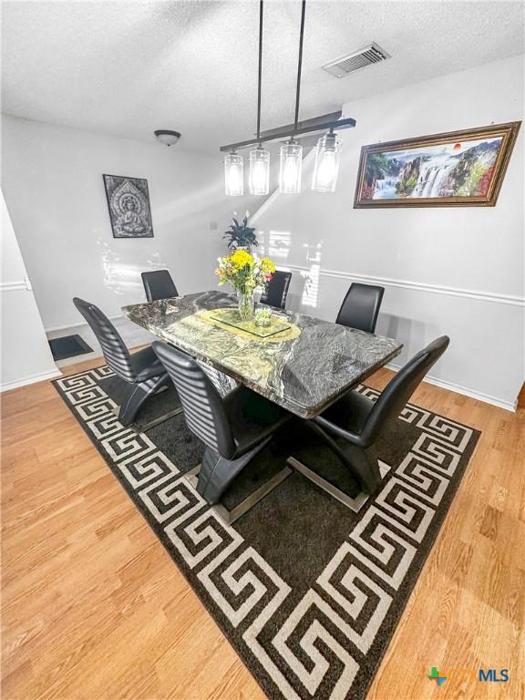 dining room featuring a textured ceiling, wood finished floors, visible vents, and baseboards