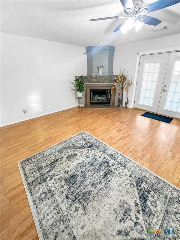living room featuring visible vents, a fireplace with raised hearth, a textured ceiling, and wood finished floors