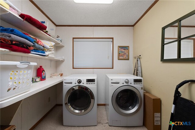 clothes washing area with washing machine and dryer, a textured ceiling, crown molding, and light carpet