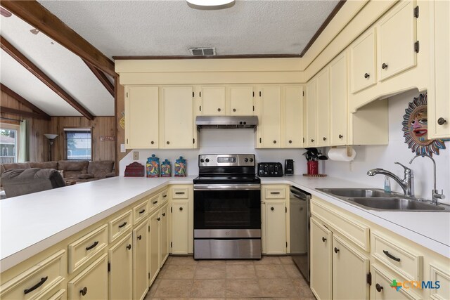 kitchen with stainless steel appliances, cream cabinetry, wooden walls, and sink