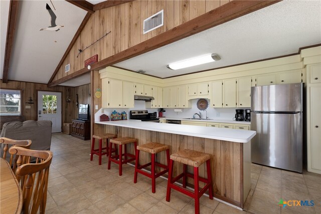 kitchen with stainless steel appliances, beam ceiling, wood walls, sink, and kitchen peninsula