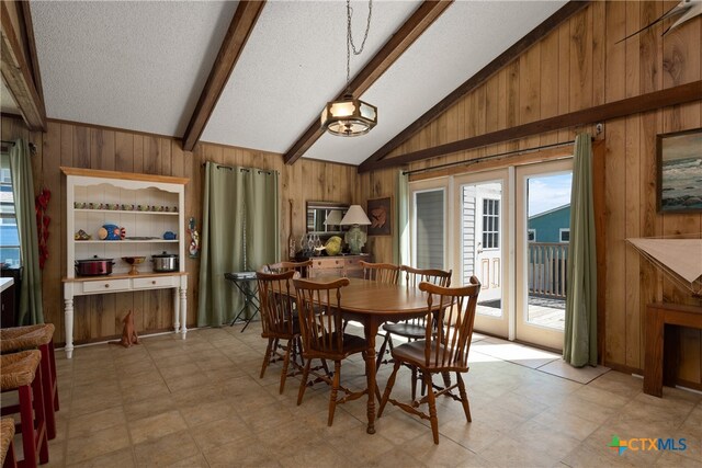 dining area featuring wood walls, a textured ceiling, and vaulted ceiling with beams