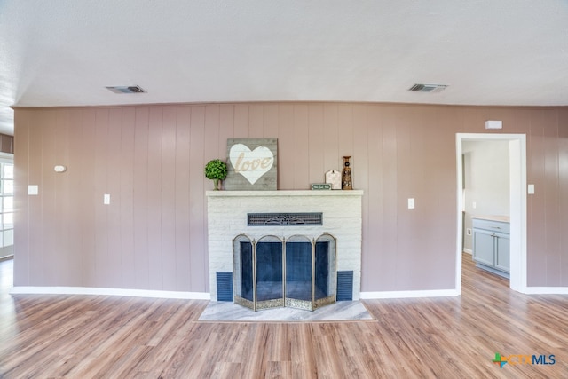 unfurnished living room with a textured ceiling, light hardwood / wood-style flooring, and wooden walls