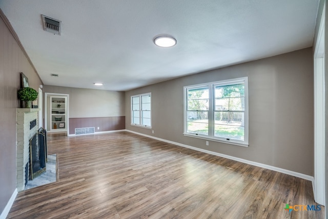 unfurnished living room with built in shelves, a textured ceiling, hardwood / wood-style flooring, and a fireplace