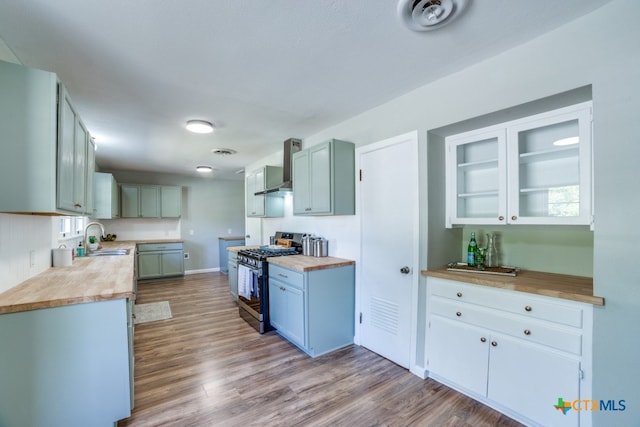 kitchen featuring wooden counters, light wood-type flooring, sink, stainless steel range with gas stovetop, and wall chimney exhaust hood