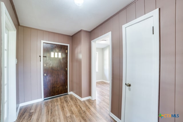 entryway with light hardwood / wood-style floors, wood walls, a textured ceiling, and crown molding