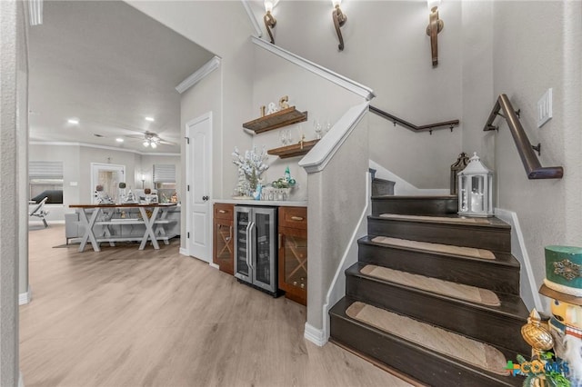 stairway with hardwood / wood-style floors, bar area, crown molding, ceiling fan, and beverage cooler