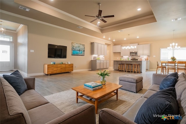 living room featuring light wood-type flooring, a tray ceiling, ceiling fan with notable chandelier, and crown molding