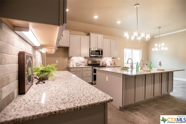 kitchen featuring pendant lighting, light stone counters, a kitchen island with sink, white cabinetry, and appliances with stainless steel finishes