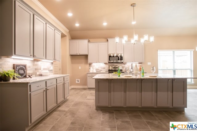 kitchen with a kitchen island with sink, appliances with stainless steel finishes, decorative light fixtures, and light stone countertops