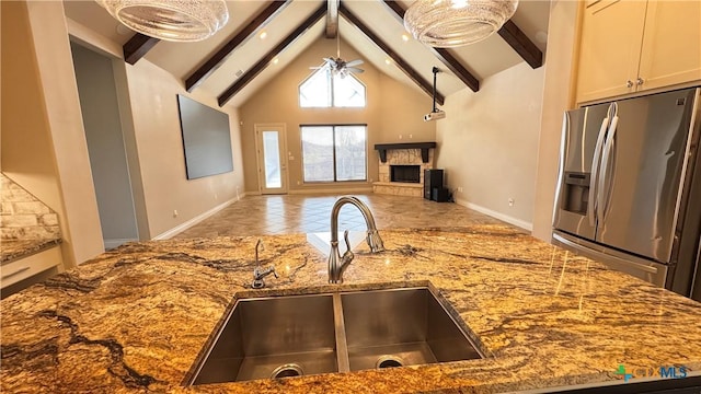 kitchen featuring beam ceiling, sink, a stone fireplace, and stainless steel refrigerator with ice dispenser