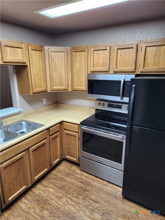 kitchen featuring stainless steel appliances, wood finished floors, a sink, and light countertops