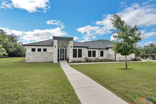 prairie-style house featuring stucco siding, fence, stone siding, and a front lawn