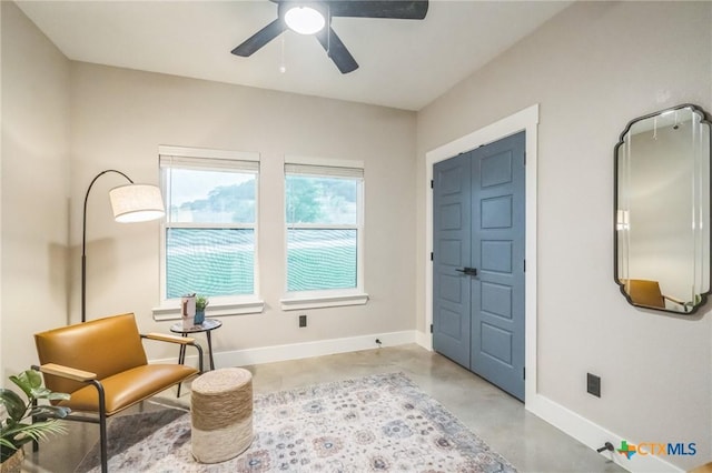 living area featuring baseboards, ceiling fan, and finished concrete floors
