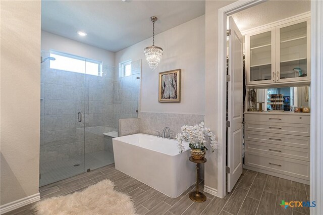 full bath featuring wood finish floors, a stall shower, a freestanding bath, and a chandelier