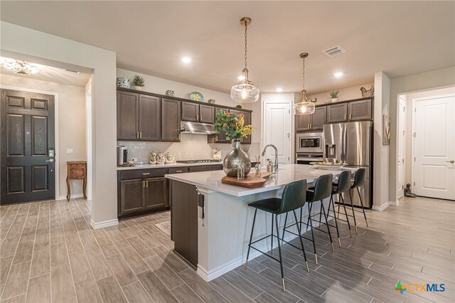 kitchen featuring pendant lighting, appliances with stainless steel finishes, a kitchen breakfast bar, a kitchen island with sink, and dark brown cabinets