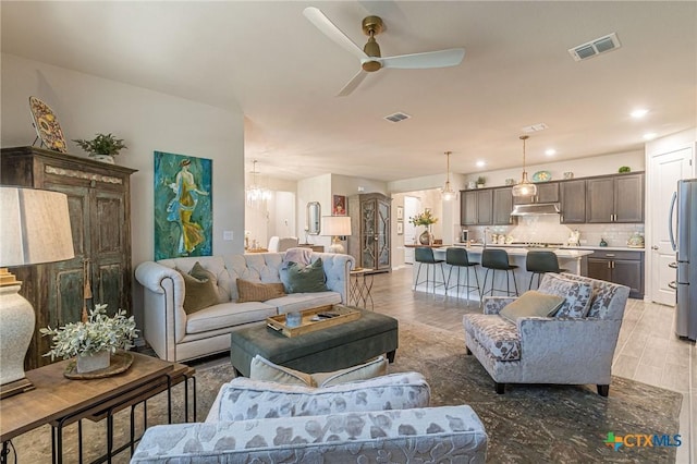 living room featuring light wood-type flooring and ceiling fan with notable chandelier