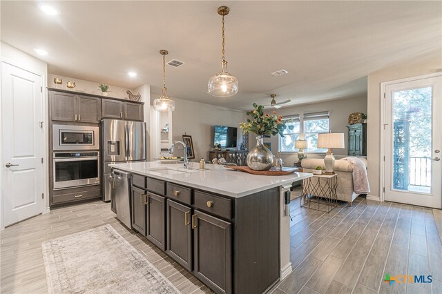 kitchen featuring appliances with stainless steel finishes, a kitchen island with sink, dark brown cabinets, hanging light fixtures, and sink