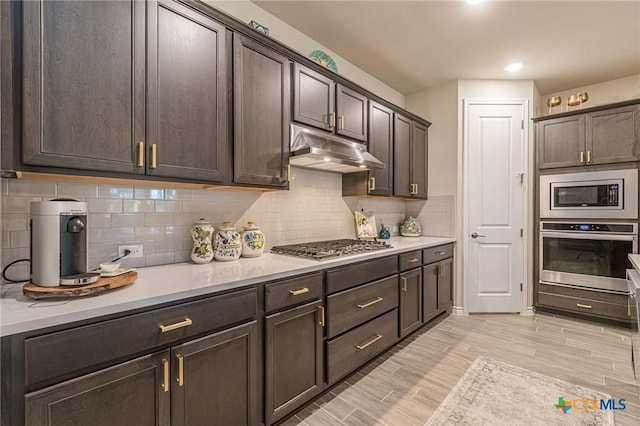 kitchen featuring stainless steel appliances, under cabinet range hood, light countertops, dark brown cabinetry, and light wood finished floors