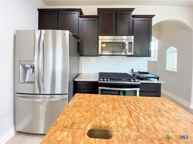 414 Field Corn Ln, San Marcos, TX 78666 - kitchen with appliances with stainless steel finishes, wooden counters, dark brown cabinets, decorative backsplash, and arched walkways