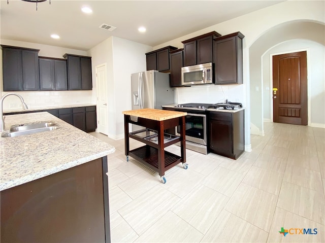 414 Field Corn Ln, San Marcos, TX 78666 - kitchen with appliances with stainless steel finishes, backsplash, light stone counters, arched walkways, and dark brown cabinets