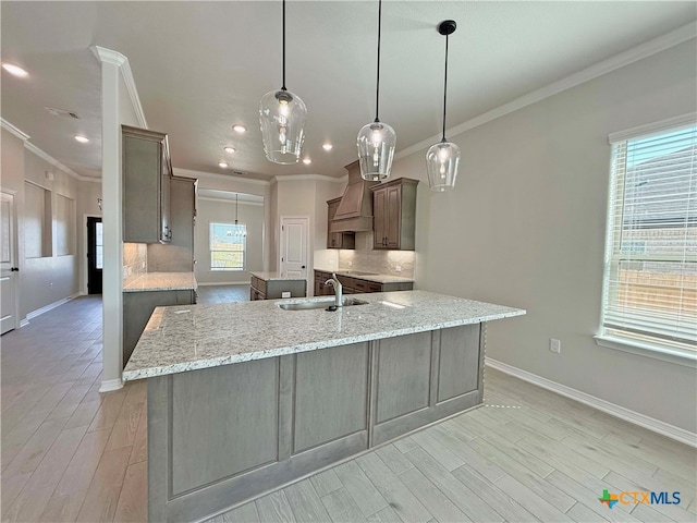 kitchen with tasteful backsplash, decorative light fixtures, light stone countertops, sink, and custom exhaust hood