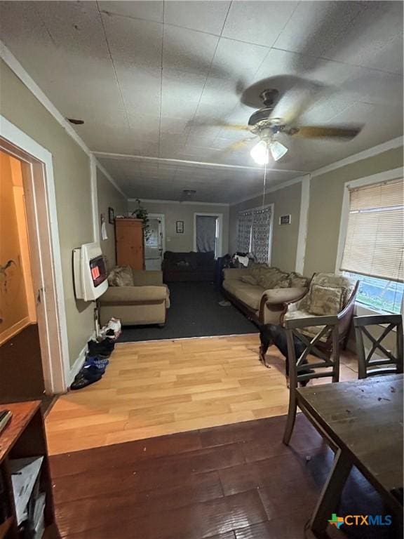 living area with heating unit, a ceiling fan, ornamental molding, and wood finished floors