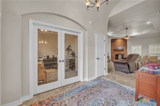 interior space featuring french doors, ceiling fan with notable chandelier, light tile patterned floors, a fireplace, and a tray ceiling