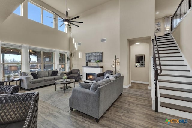 living room with a glass covered fireplace, wood finished floors, visible vents, and ceiling fan