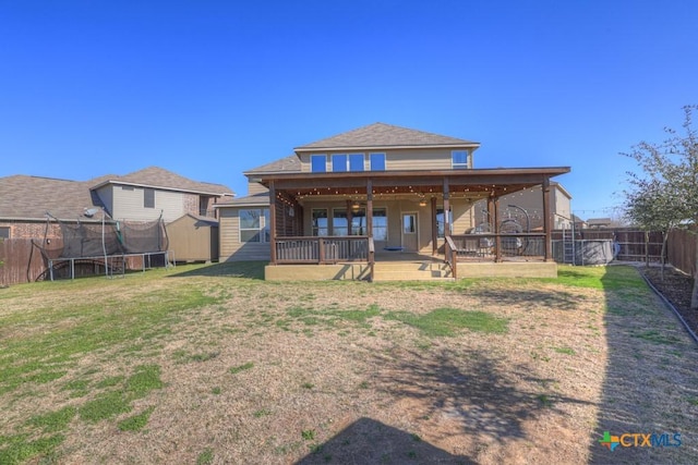 back of house featuring a trampoline, a lawn, and a fenced backyard