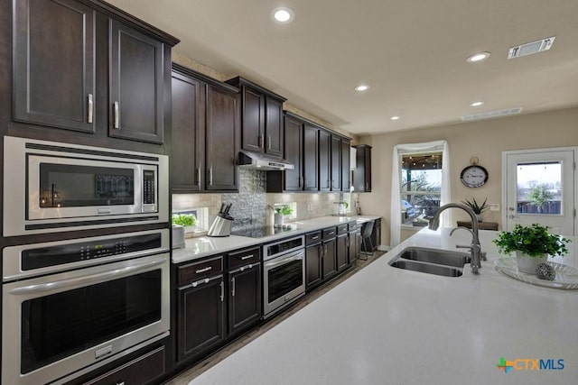 kitchen featuring visible vents, a sink, under cabinet range hood, stainless steel appliances, and light countertops