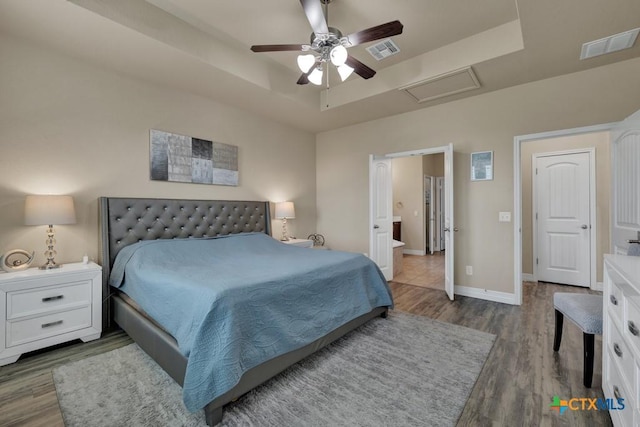 bedroom featuring visible vents, baseboards, a tray ceiling, and wood finished floors