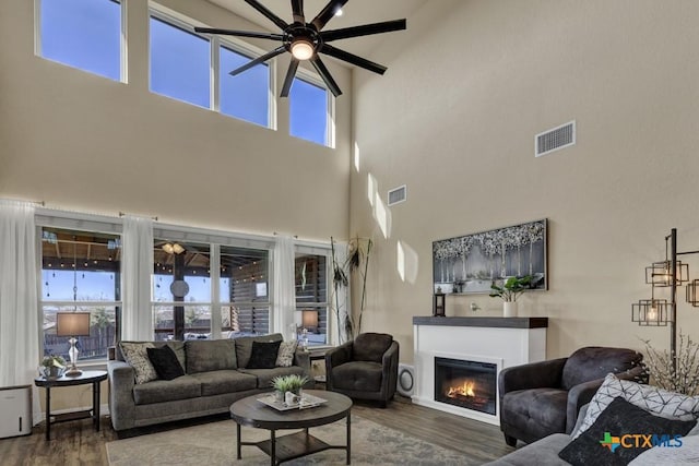 living room with a glass covered fireplace, wood finished floors, a ceiling fan, and visible vents