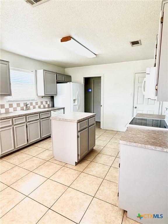 kitchen featuring light tile patterned floors, visible vents, white appliances, and a center island