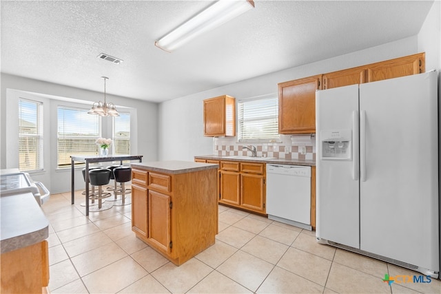 kitchen with white appliances, visible vents, a sink, decorative backsplash, and a center island