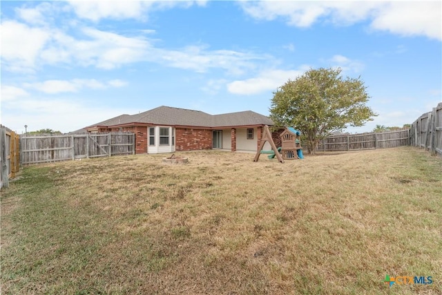 rear view of property featuring a fenced backyard, brick siding, a playground, and a yard