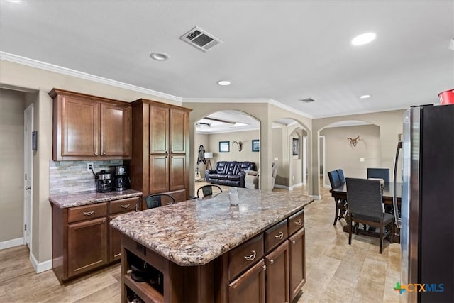 kitchen featuring a center island, crown molding, stainless steel refrigerator, light stone countertops, and backsplash