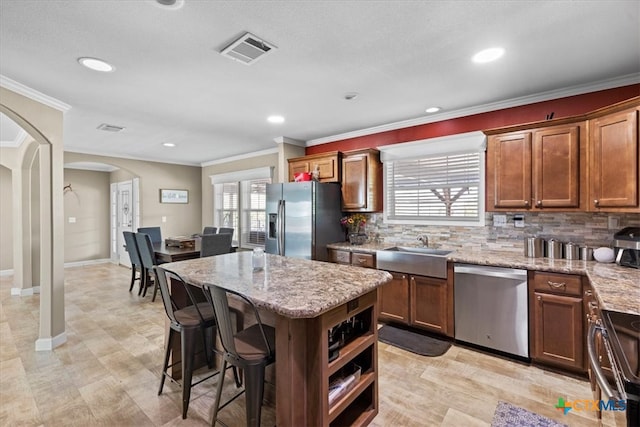 kitchen with crown molding, appliances with stainless steel finishes, a kitchen island, and backsplash