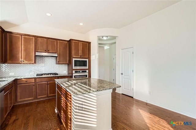 kitchen featuring dark hardwood / wood-style floors, appliances with stainless steel finishes, tasteful backsplash, a kitchen island, and light stone counters