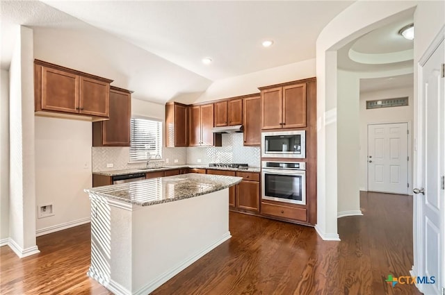 kitchen featuring light stone countertops, a center island, sink, vaulted ceiling, and appliances with stainless steel finishes