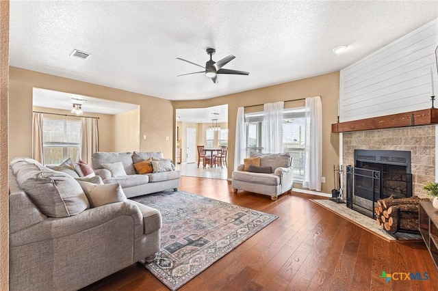 living room with a tiled fireplace, ceiling fan, dark hardwood / wood-style flooring, and a textured ceiling