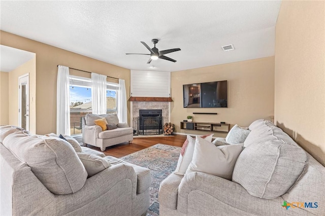 living room with ceiling fan, a fireplace, hardwood / wood-style floors, and a textured ceiling