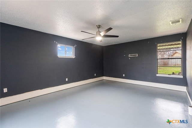 spare room with concrete flooring, a textured ceiling, visible vents, baseboards, and a ceiling fan