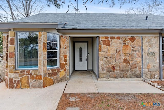 entrance to property with stone siding and a shingled roof