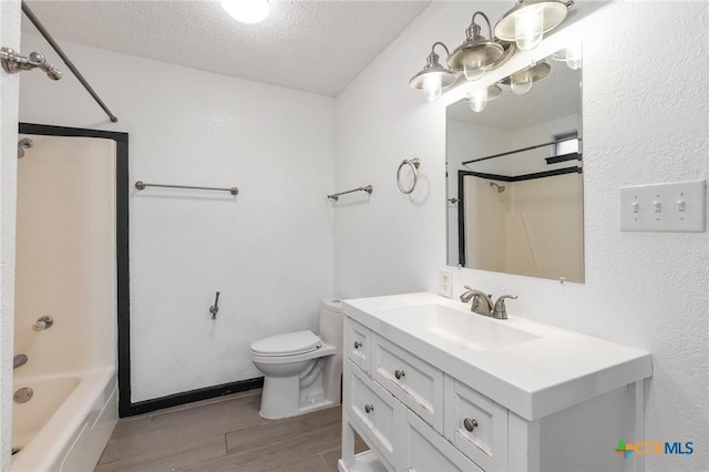 bathroom with a textured ceiling, toilet, wood finished floors, vanity, and shower / bathing tub combination