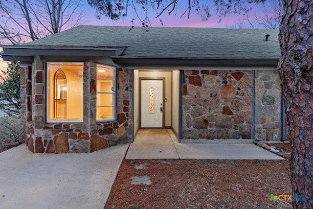 view of front of property with stone siding and roof with shingles