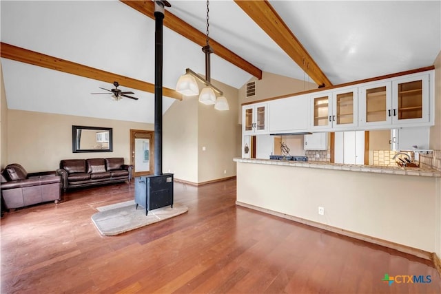 living room featuring vaulted ceiling with beams, ceiling fan, hardwood / wood-style flooring, and a wood stove